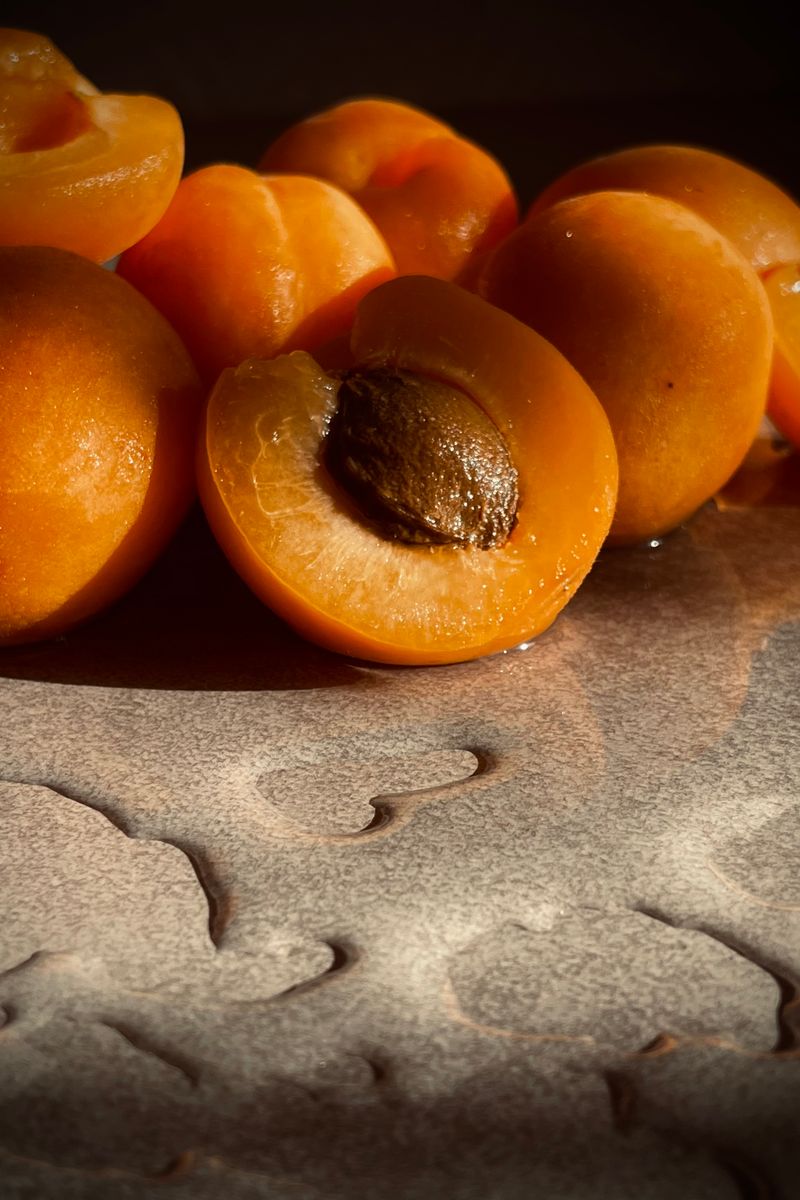 A close-up of fresh, sliced apricots showcasing their seeds on a textured table under sunlight.