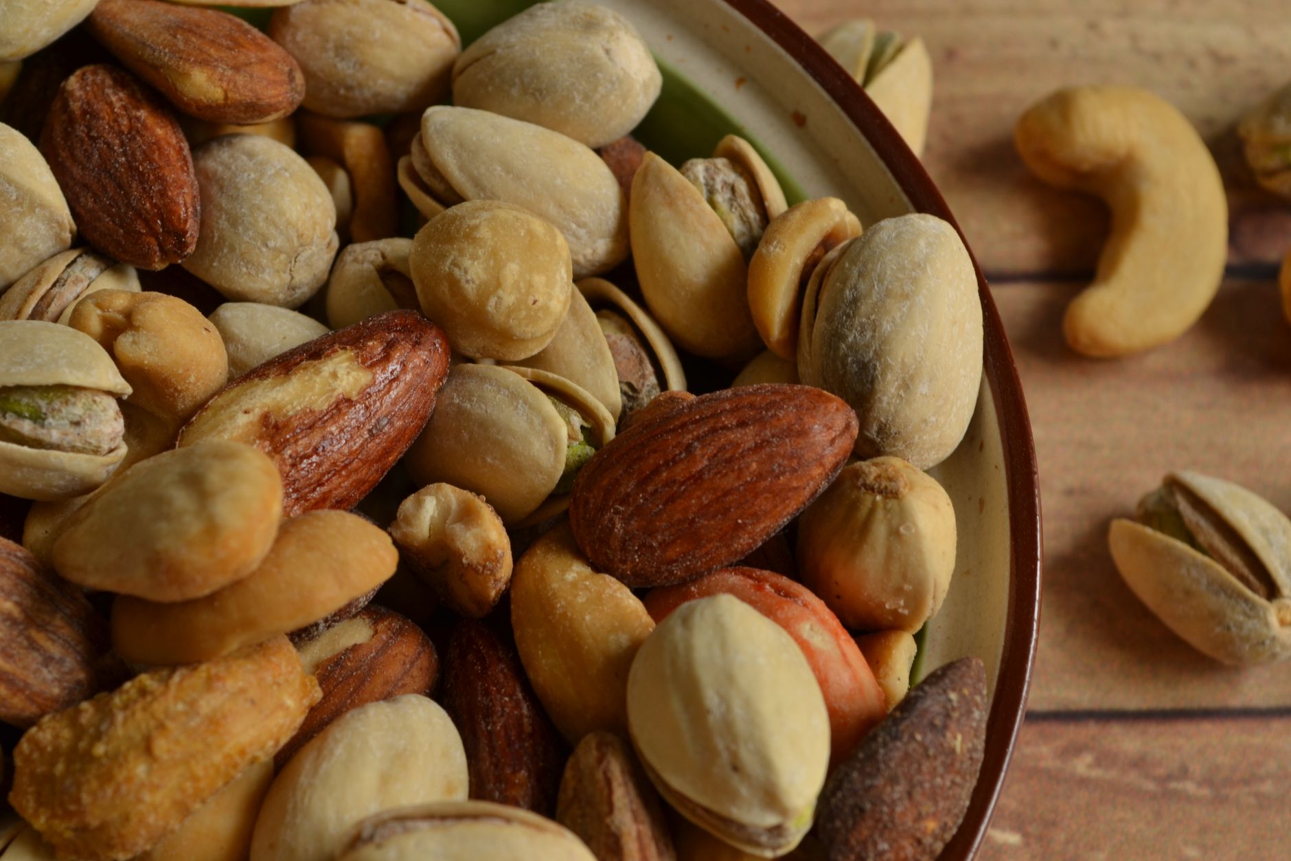 A detailed view of assorted almonds, cashews, and pistachios in a rustic bowl.